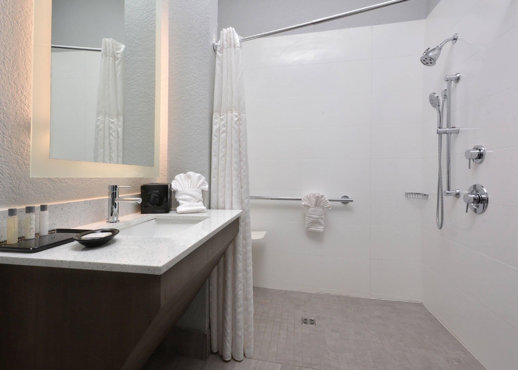 A modern bathroom with a large mirror, a vanity with a sink, a shower area, and a towel rack.