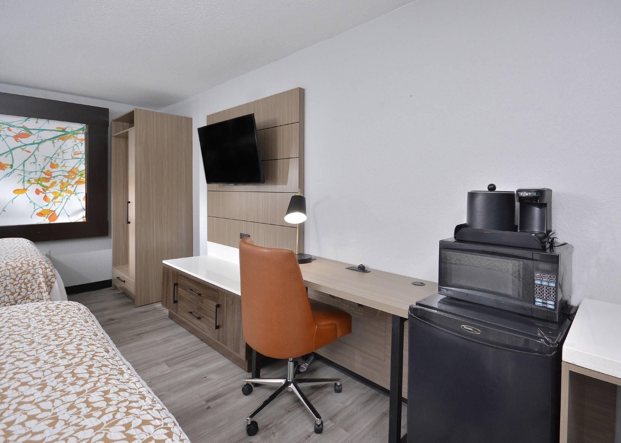 Habitación de hotel con cama, escritorio con silla, televisión, cafetera y microondas.