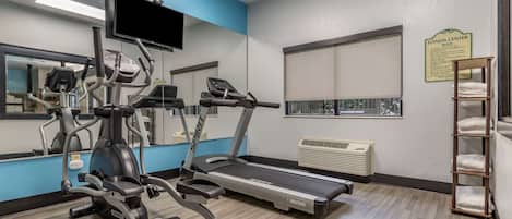 Un gimnasio con cintas de correr, elípticas y un espejo grande.