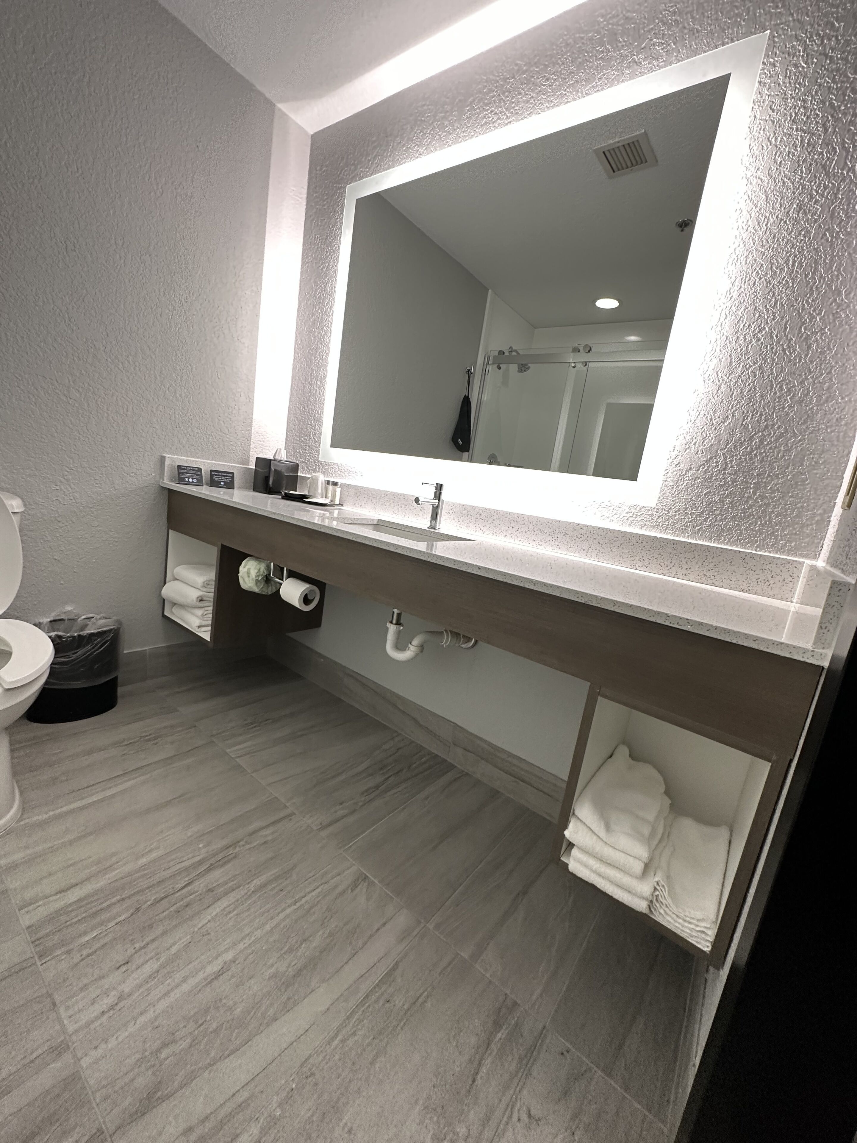 A modern bathroom with a large mirror, a sink, and a toilet.