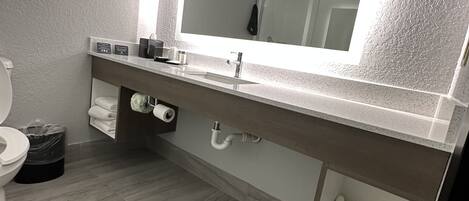 A modern bathroom with a large mirror, a sink, and a toilet.