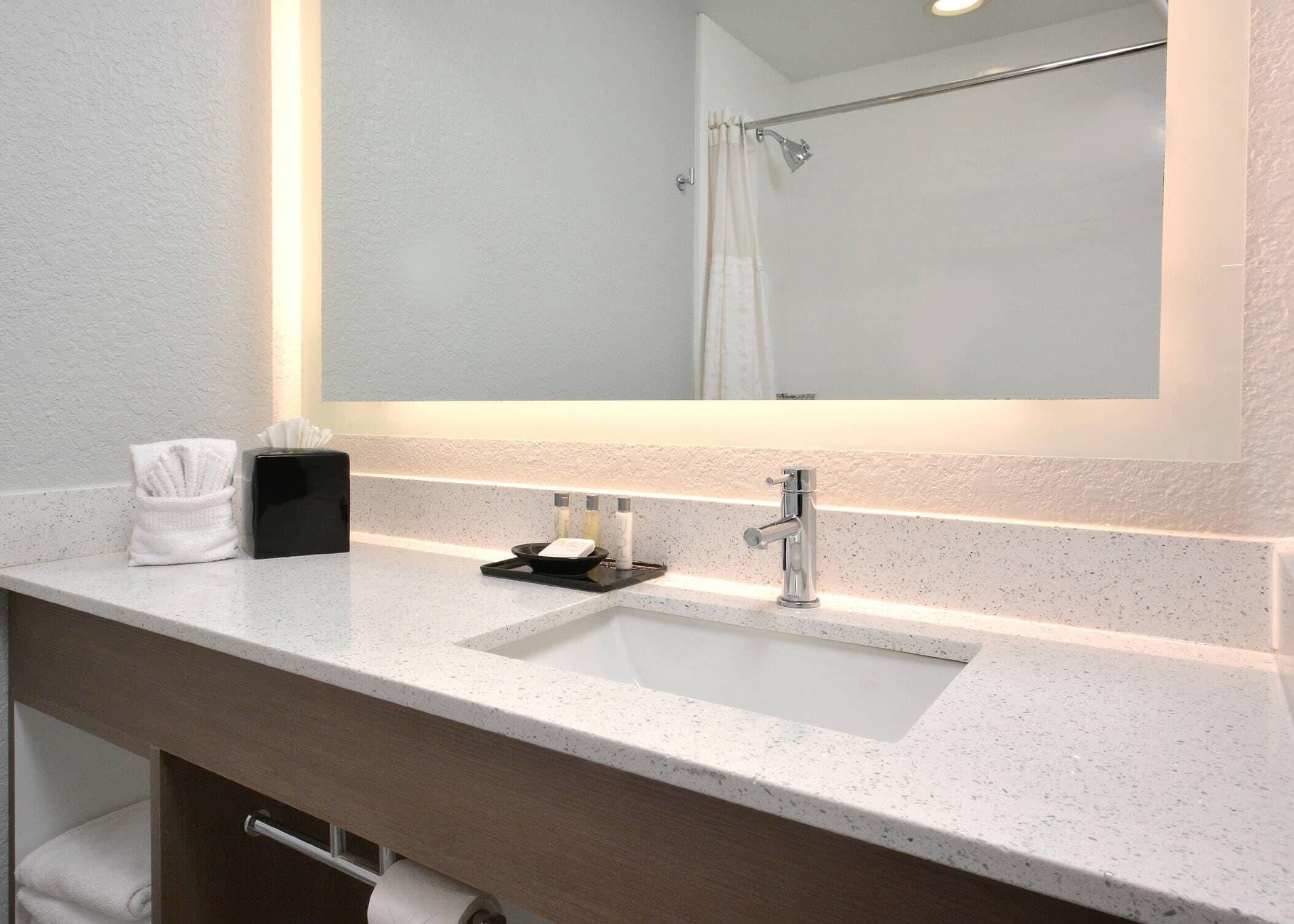 Une salle de bain avec un comptoir blanc, un lavabo, un miroir, un porte-serviettes et un rideau de douche.