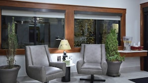 A lobby with two grey armchairs, a small round table with a lamp, and potted plants.