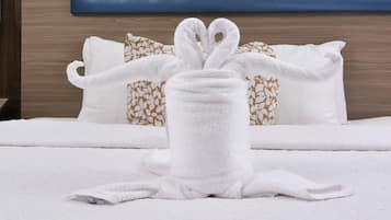 A neatly made bed with white bedding and a towel arranged in a bunny shape.