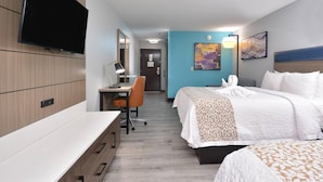A hotel room with a bed, desk, chair, and a flat-screen TV.