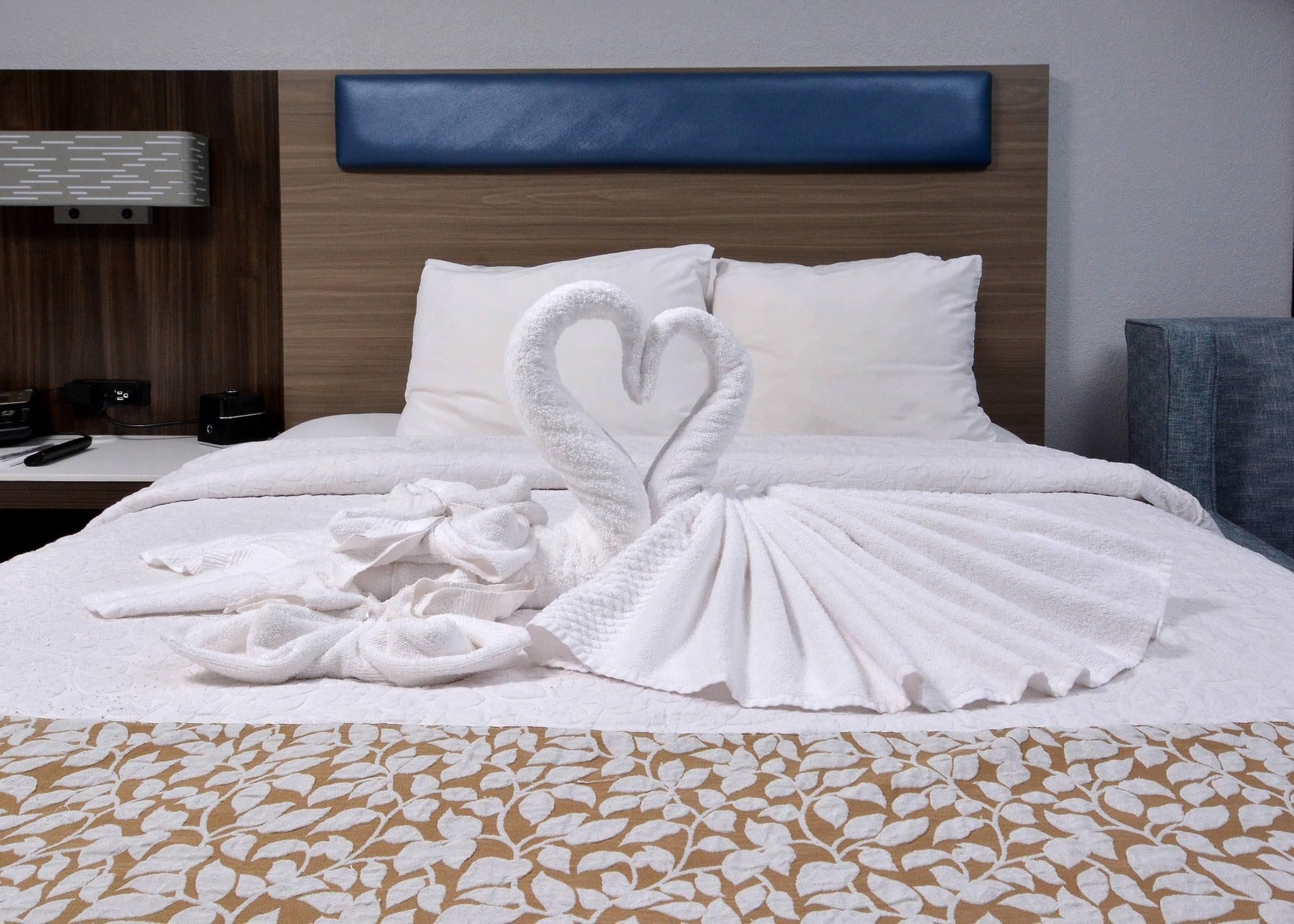 A hotel room with a neatly made bed featuring a heart-shaped towel arrangement.
