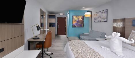 Habitación de hotel con cama, escritorio con silla, televisor, un cuadro y la puerta del baño.