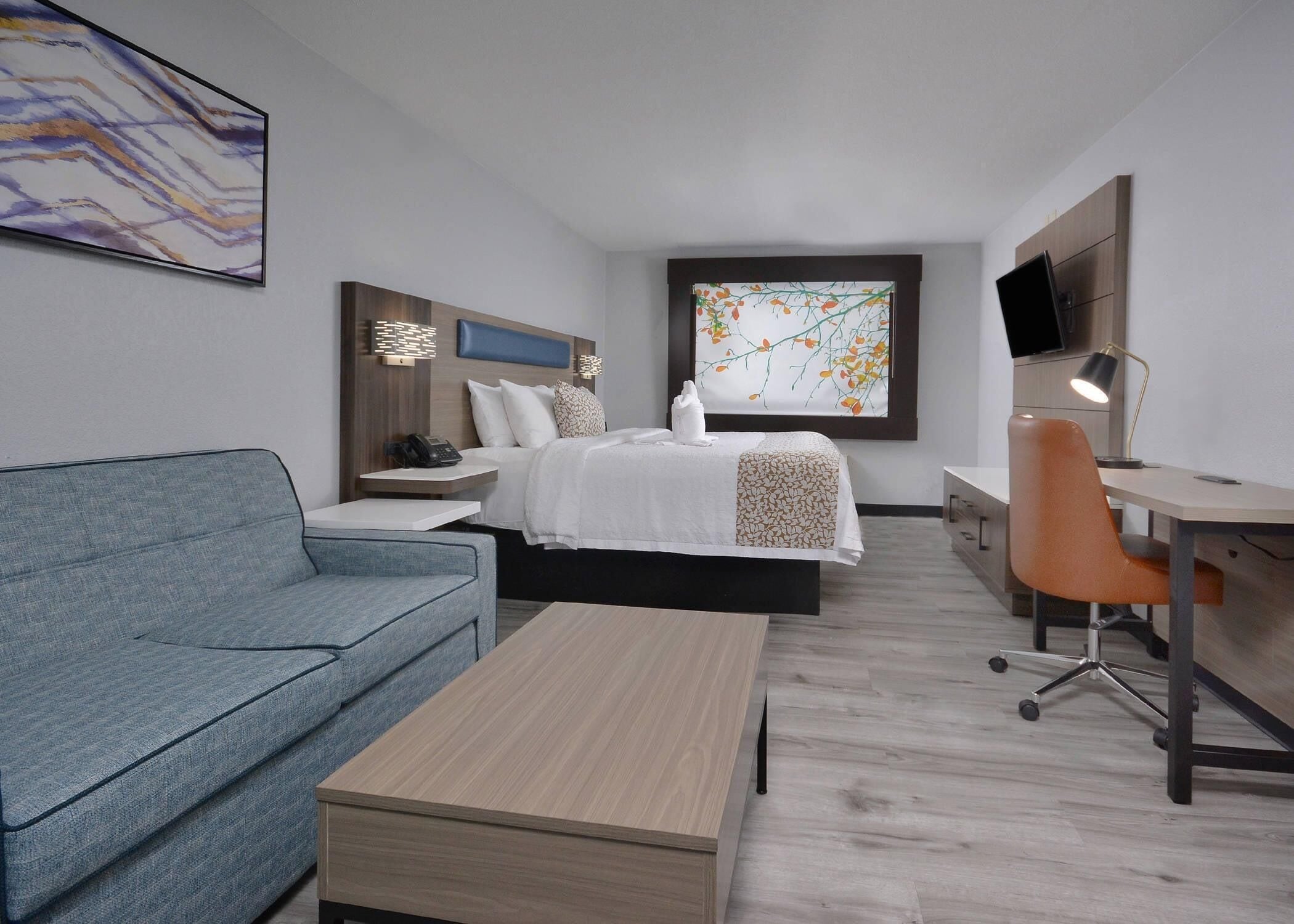 A modern hotel room with a bed, a desk, a chair, a sofa, and a TV.