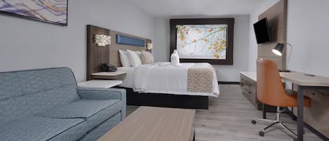 A modern hotel room with a bed, a desk, a chair, a sofa, and a TV.