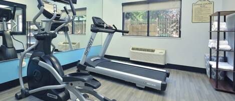 Un gimnasio con cintas de correr, una elíptica y un espejo grande.