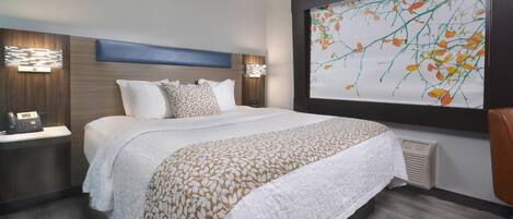 A modern hotel room with a large bed, two bedside tables with lamps, a telephone, and a large window with a floral view.
