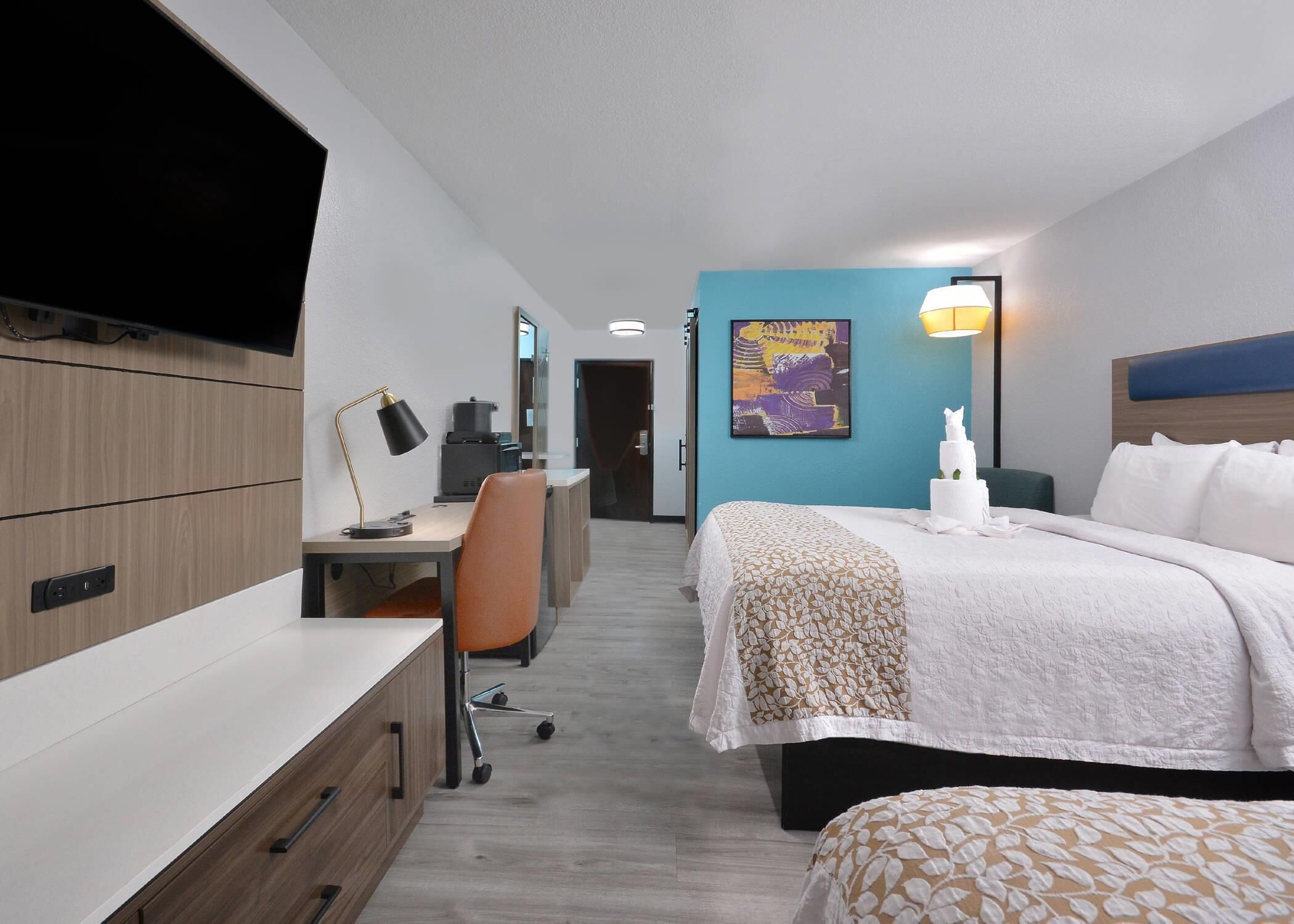 Une chambre d’hôtel équipée d’un bureau, d’une chaise, d’un lit et d’un téléviseur fixé au mur.