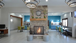 A modern living room with a stone fireplace, seating area, and a kitchen in the background.