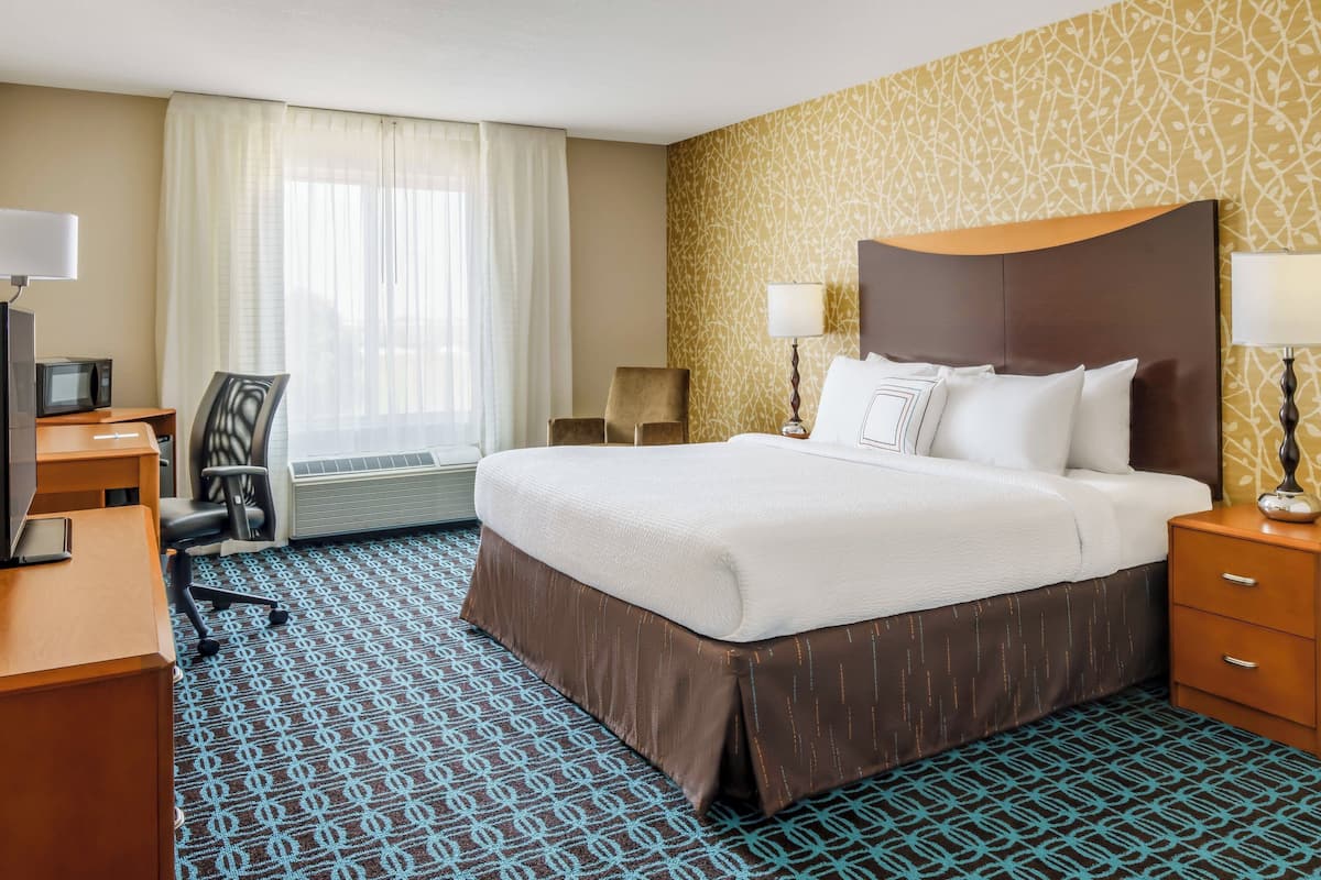 Una habitación de hotel con una cama grande, un escritorio con computadora, una silla y un televisor.