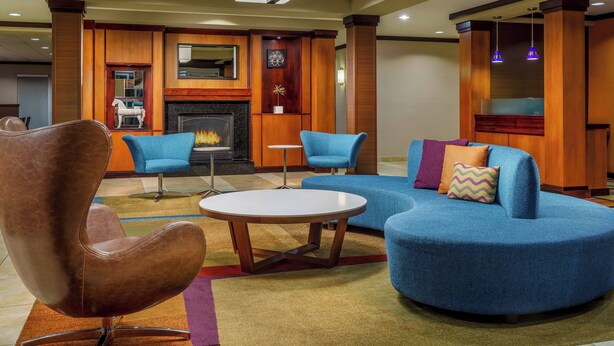 Een moderne lobby met een open haard, blauwe banken, een bruine stoel en een ronde tafel.