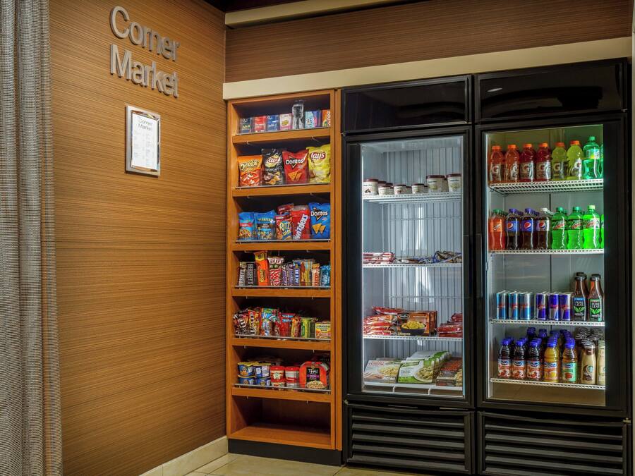 A corner market with shelves stocked with snacks and a refrigerated display with beverages.