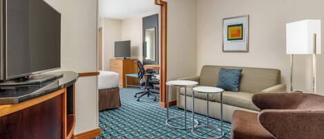 A hotel room with a flat-screen TV, a sofa, a small table, a desk, and a chair.