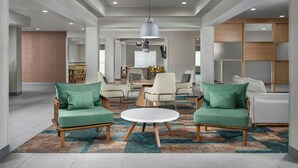 A modern living room with a round coffee table, two green armchairs, a dining area with a table and chairs, and a large wooden bookshelf. - Fairfield Inn & Suites by Marriott Dallas Mansfield (Mansfield)