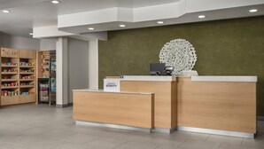 A hotel reception desk with a 'Marriott Bonvoy' sign, a refrigerator, and a 'Market' section with shelves of products. - Fairfield Inn & Suites by Marriott Dallas Mansfield (Mansfield)