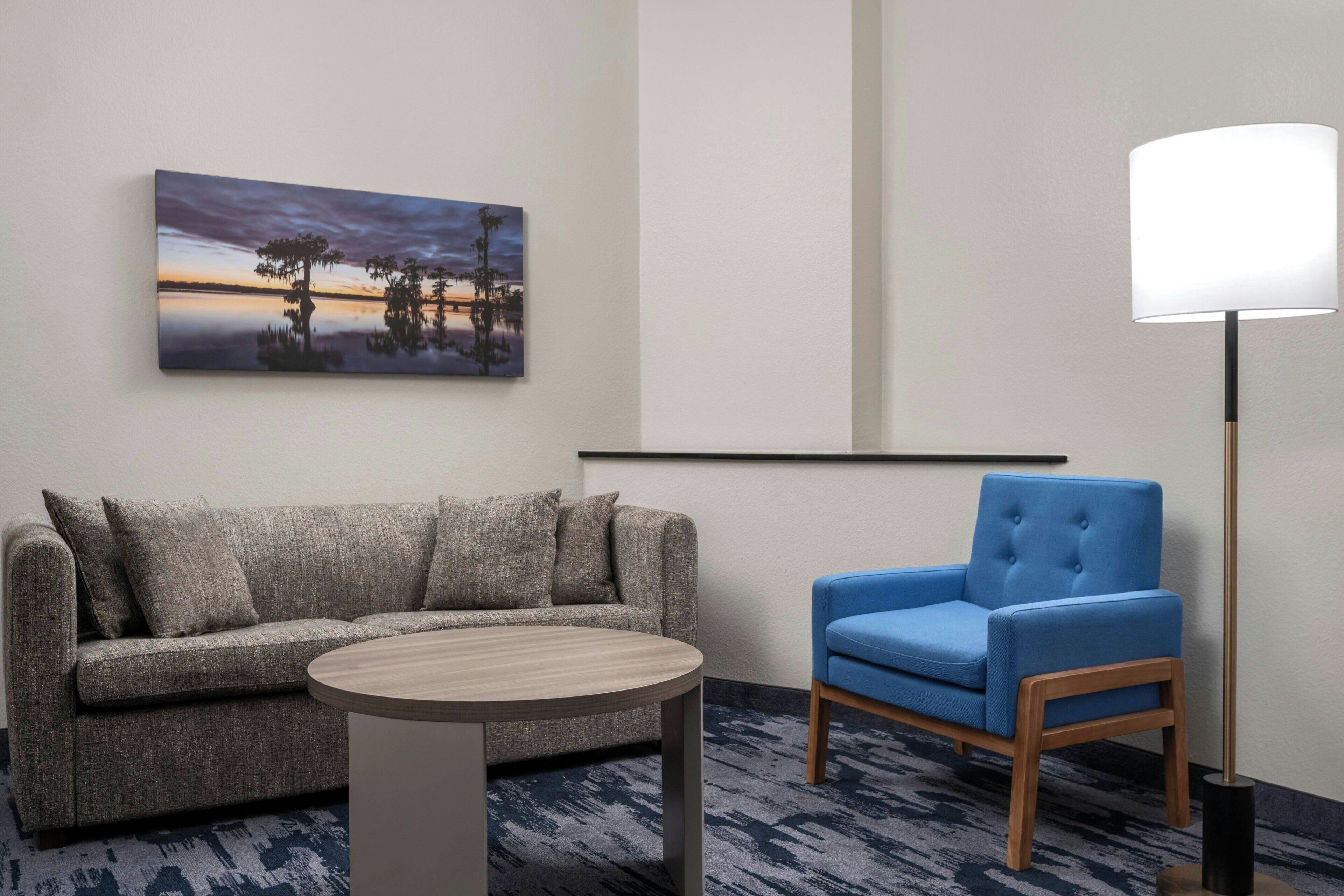 Una habitación moderna con un sofá gris, una mesa redonda de madera, un sillón azul y una lámpara de pie.