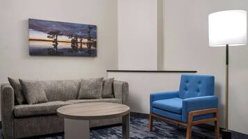 Una habitación moderna con un sofá gris, una mesa redonda de madera, un sillón azul y una lámpara de pie.