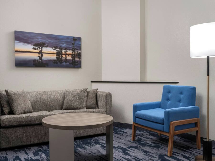 Una habitación moderna con un sofá gris, una mesa redonda de madera, un sillón azul y una lámpara de pie.