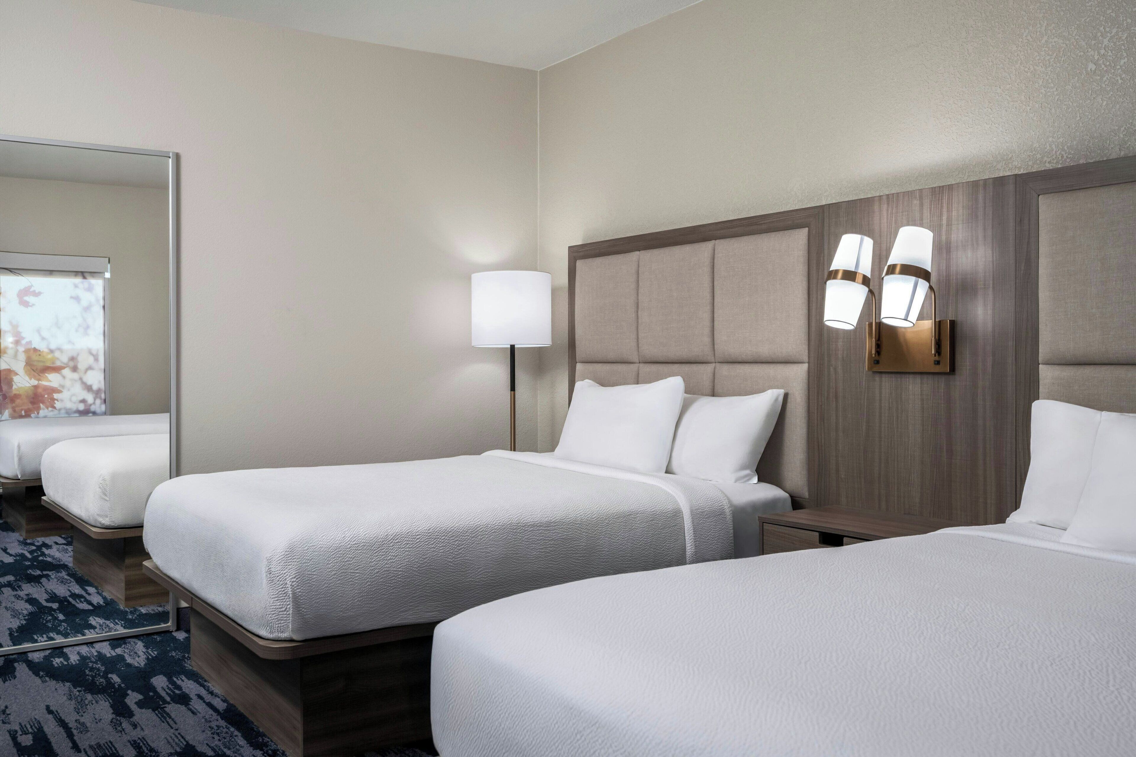 A hotel room with two single beds, a nightstand, a lamp, and a large mirror.