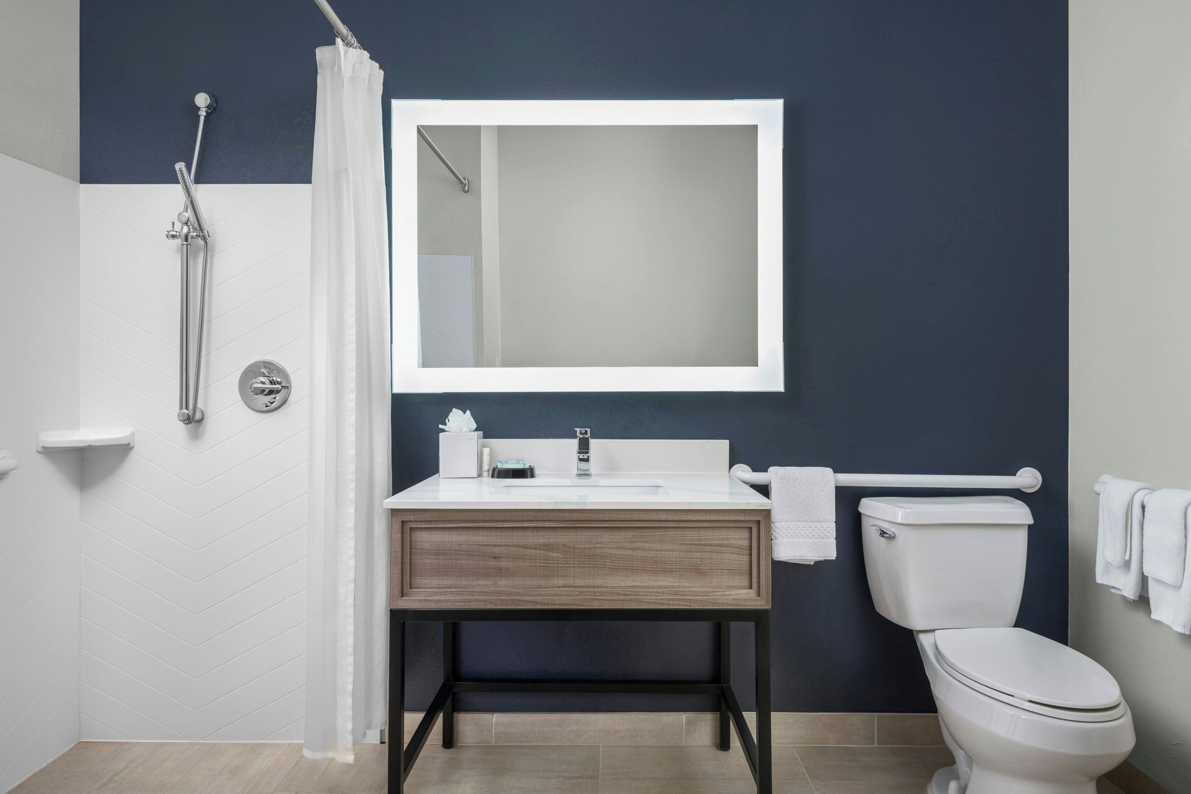 A modern bathroom with a white sink, a mirror, a toilet, and a shower area.
