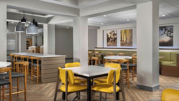 A modern restaurant with high ceilings, pendant lighting, and a mix of wooden and upholstered furniture. - Fairfield Inn & Suites by Marriott Dallas Mansfield (Mansfield)