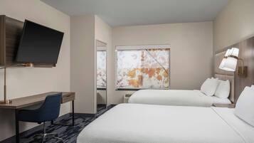 A hotel room with a bed, a desk, a chair, a TV, and a window with a view of autumn leaves.