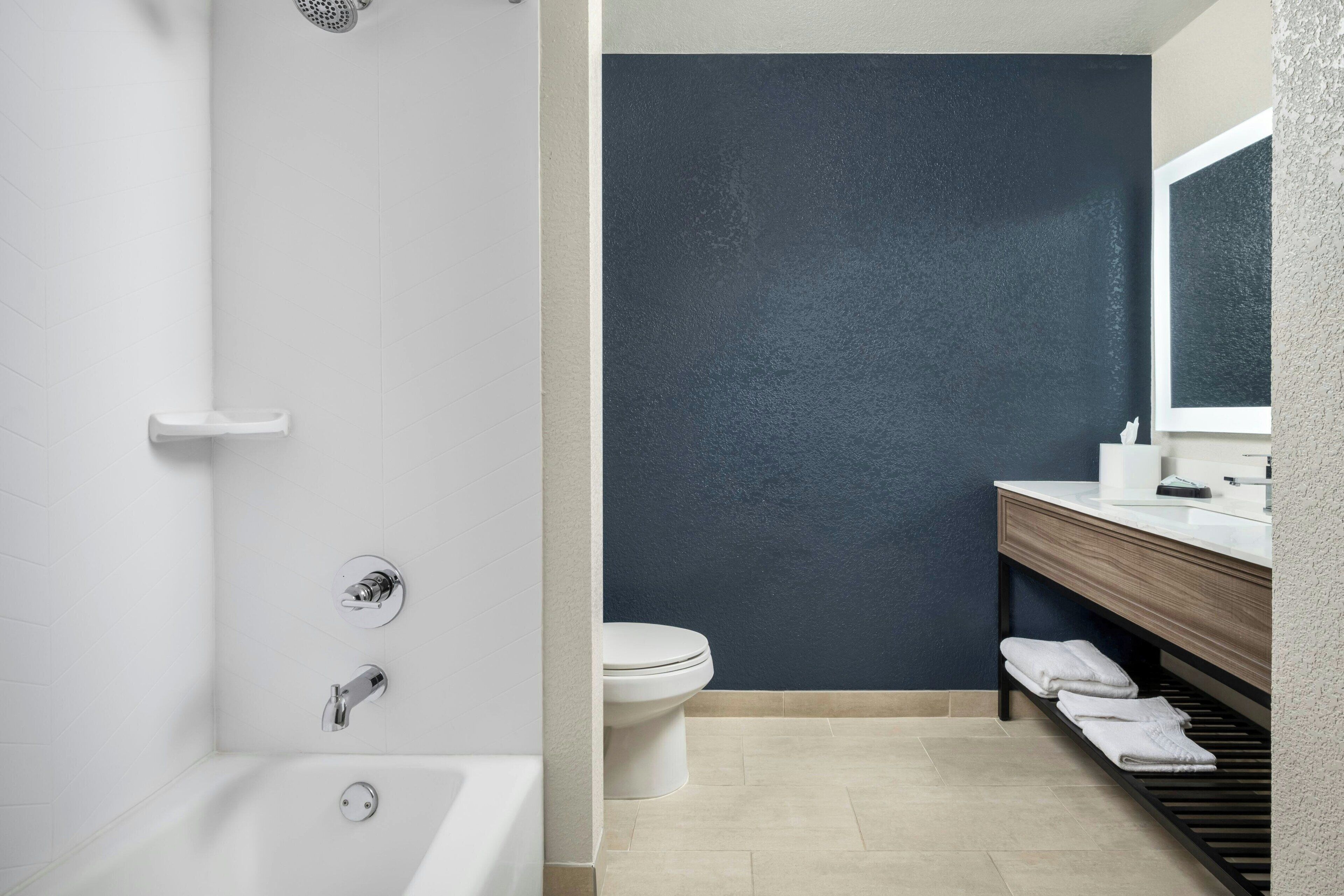 Un baño moderno con una bañera blanca, un inodoro y una pared de acento azul oscuro.