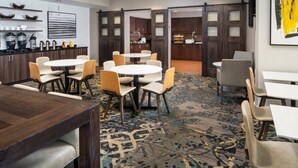 A hotel lobby with a central round table surrounded by chairs, a coffee station, and a view into the kitchen area. - Residence Inn by Marriott New Orleans Covington/North Shore (Covington)