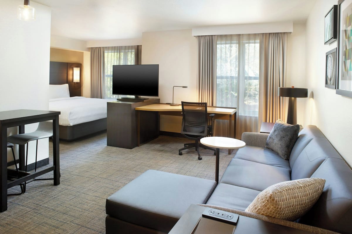 A hotel room with a bed, a desk with a computer, a sofa, and a TV.