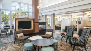 A spacious indoor area with a fireplace, comfortable seating, and large windows offering views of the outdoors. - Residence Inn by Marriott New Orleans Covington/North Shore (Covington)