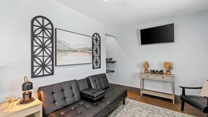 A modern living room with a black leather sofa, a mounted TV, decorative wall art, and a console table with vases.