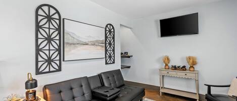 A modern living room with a black leather sofa, a mounted TV, decorative wall art, and a console table with vases.