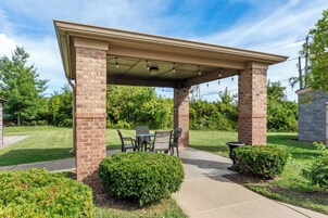 A covered patio area with a brick column structure, outdoor furniture, and well-maintained landscaping.