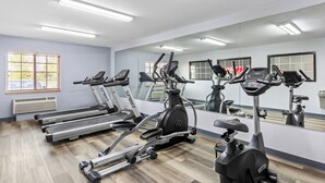 A gym with treadmills, an elliptical, and a stationary bike, with a large mirror and windows.