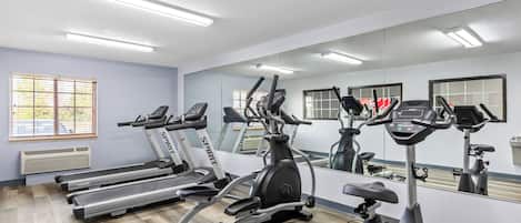 A gym with treadmills, an elliptical, and a stationary bike, with a large mirror and windows.