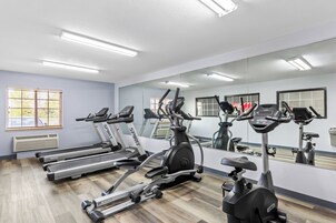 A gym with treadmills, an elliptical, and a stationary bike, with a large mirror and windows.