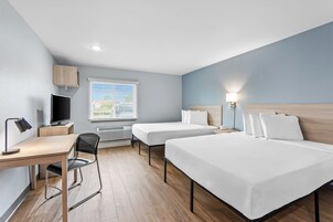 A hotel room with a desk, two beds, a TV, and a window with blinds.