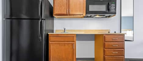 A kitchen with a black refrigerator, wooden cabinets, a microwave, and a countertop.