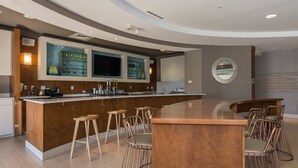 A modern kitchen with a curved island, bar stools, and a large TV.
