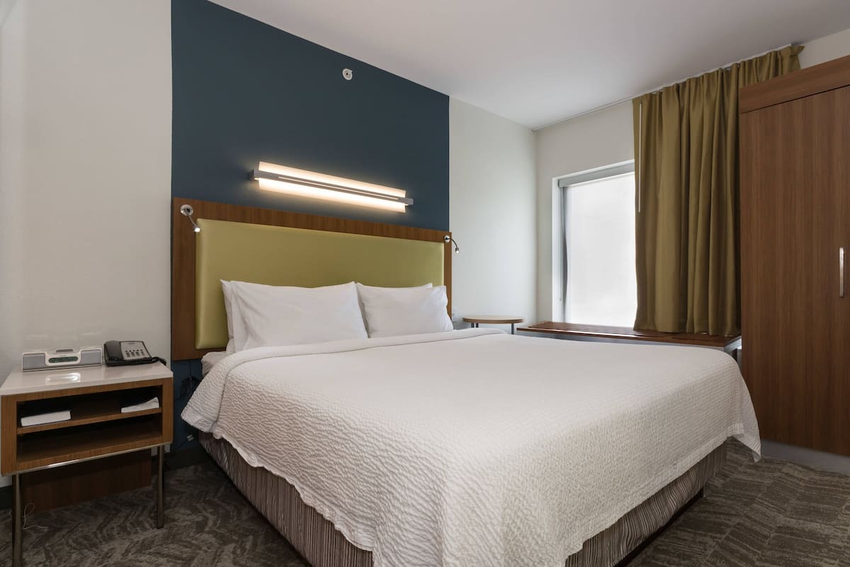 A hotel room with a large bed, a bedside table with a phone, a lamp, and a window with curtains.