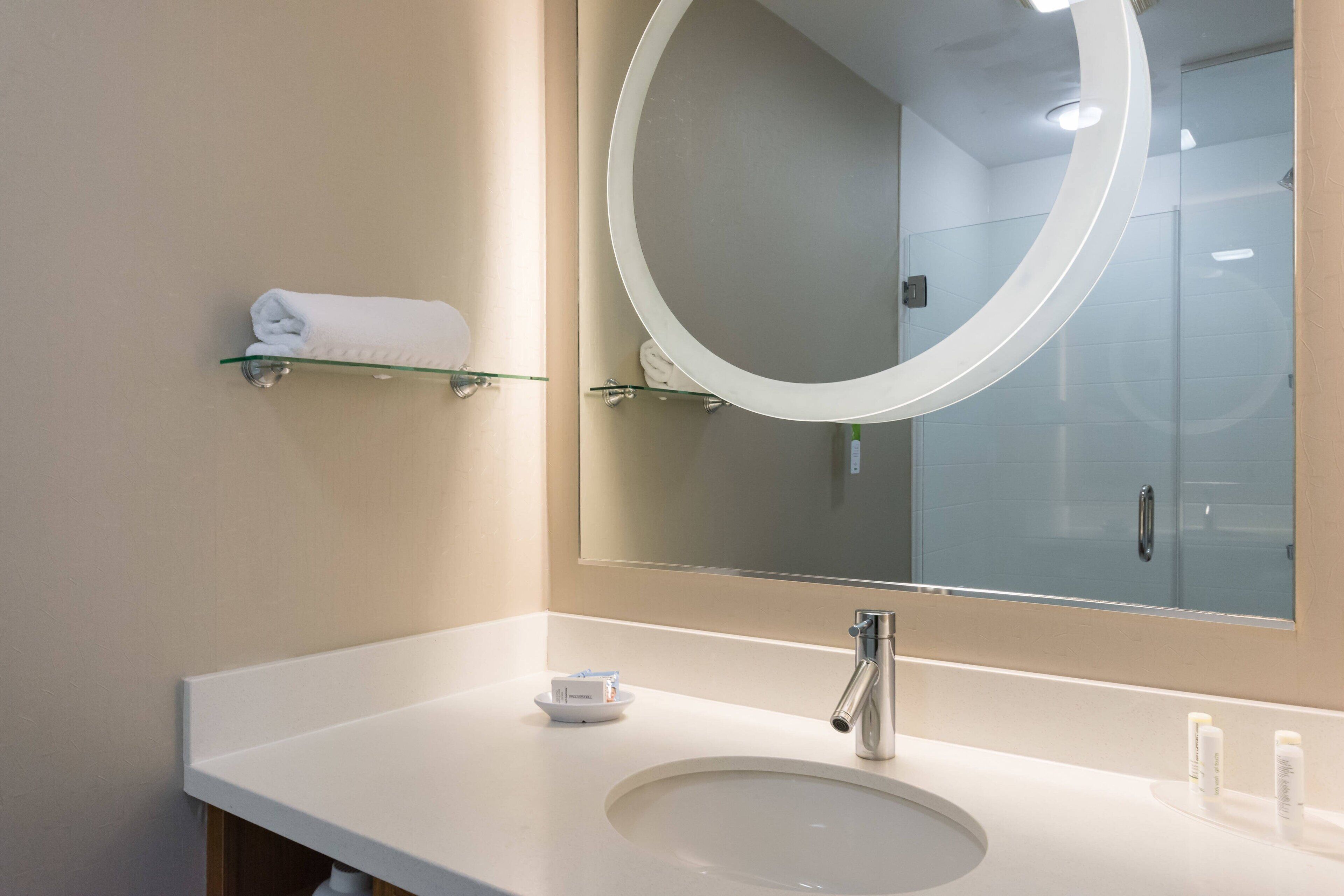 A modern bathroom with a white sink, a round mirror, and a glass shower enclosure.