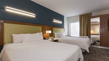 Habitación de hotel con dos camas, cabecero de madera, mesita de noche con lámpara y un ventanal con cortinas.