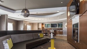 A modern lounge area with a curved seating arrangement, a central round table, and a kitchen area in the background.