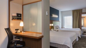 A hotel room with a desk, two beds, a chair, and a mirror.