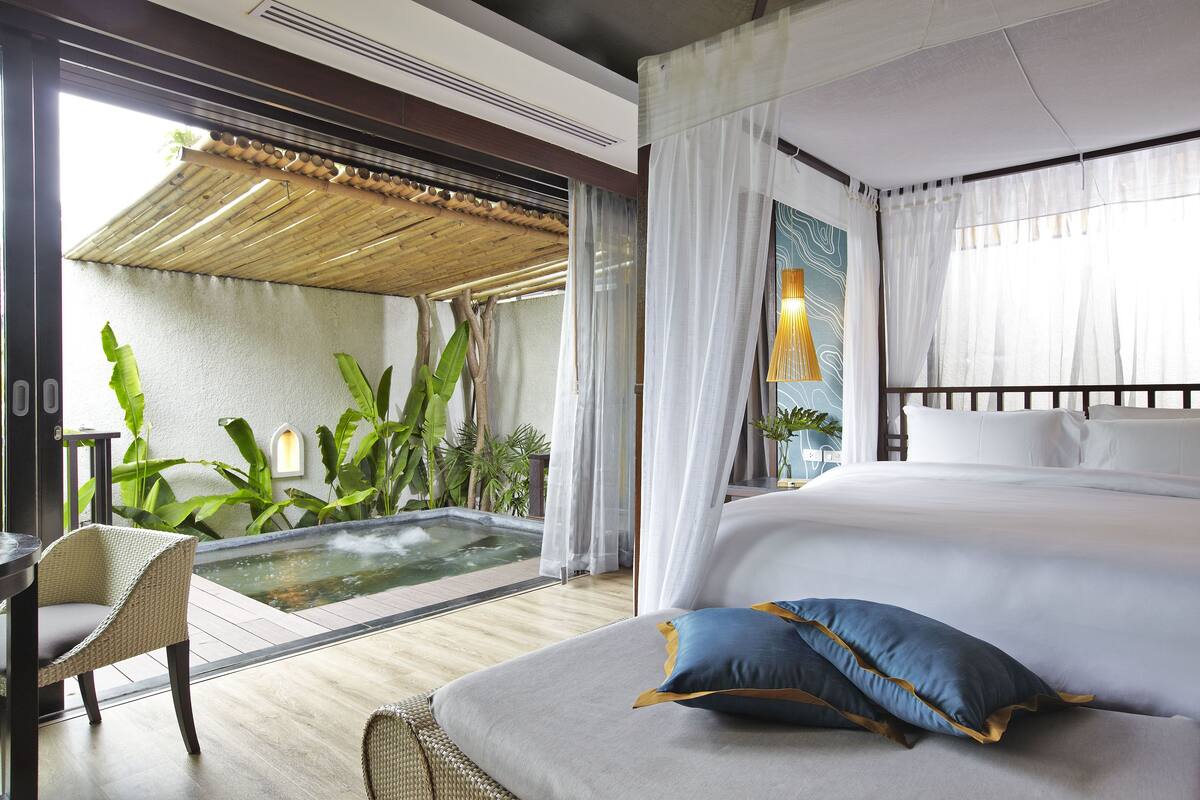 A bedroom with a large bed, a small table, and a hot tub.