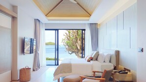 Un dormitorio moderno con una cama grande, una silla, una mesita de noche y vistas al mar.